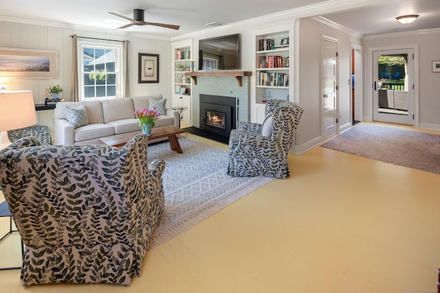 living room featuring crown molding, ceiling fan, a brick fireplace, built in shelves, and baseboards