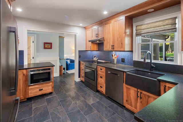 kitchen with appliances with stainless steel finishes, dark countertops, a sink, under cabinet range hood, and recessed lighting