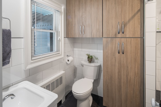 bathroom with a sink, radiator, toilet, and tile walls