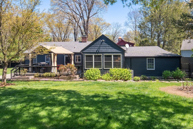 ranch-style home with a shingled roof, a front yard, a chimney, and a deck