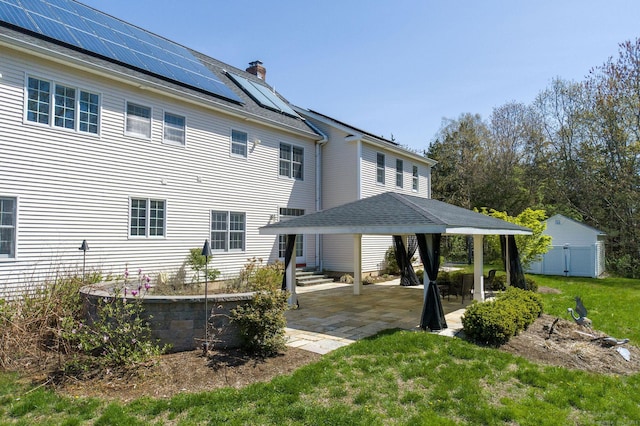 back of house featuring a gazebo, a chimney, solar panels, a patio area, and a yard