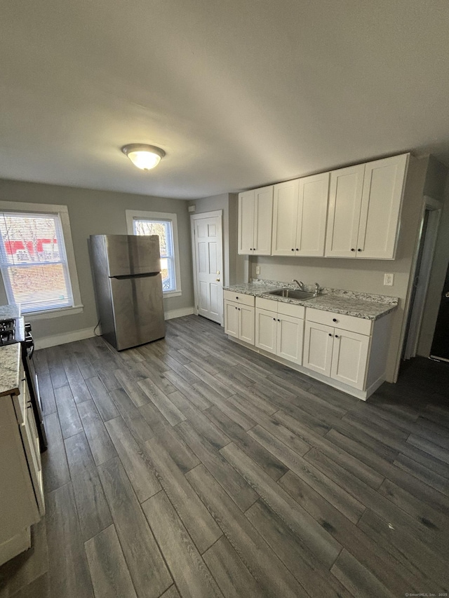kitchen featuring a sink, dark wood-style flooring, baseboards, white cabinets, and freestanding refrigerator