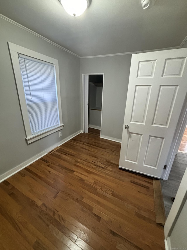 unfurnished bedroom featuring baseboards, a closet, wood-type flooring, and crown molding