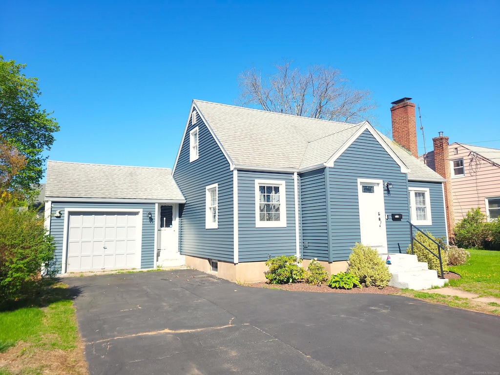view of front facade featuring driveway, roof with shingles, a chimney, and an attached garage