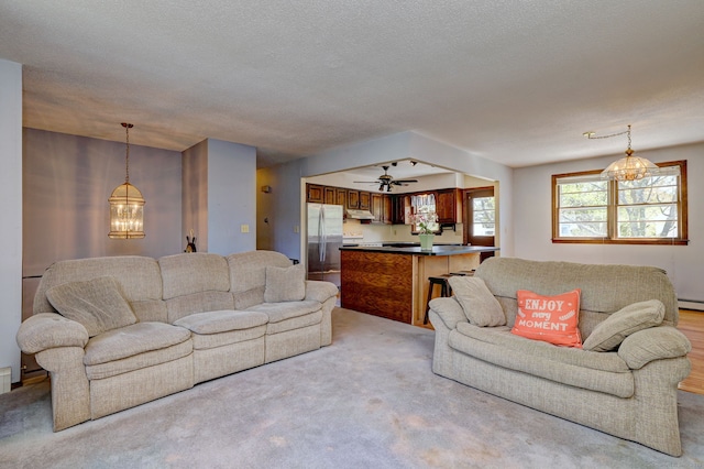 carpeted living area featuring a textured ceiling and ceiling fan with notable chandelier