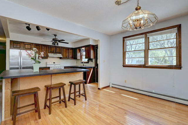 kitchen featuring dark countertops, a breakfast bar area, freestanding refrigerator, under cabinet range hood, and white electric range