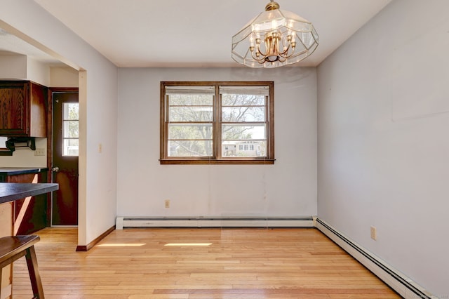 unfurnished dining area featuring a chandelier, baseboards, a baseboard heating unit, and light wood-style floors