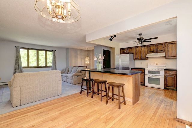 kitchen with a breakfast bar, freestanding refrigerator, range with two ovens, light wood-type flooring, and under cabinet range hood