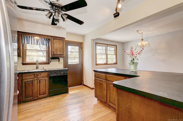 kitchen with dark countertops, dishwasher, a sink, freestanding refrigerator, and light wood-style flooring