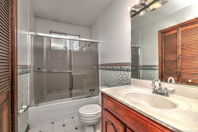 bathroom with vanity, wainscoting, toilet, tile patterned floors, and enclosed tub / shower combo