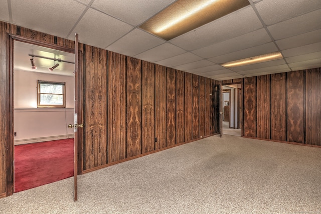 basement featuring wood walls, a drop ceiling, baseboard heating, and carpet flooring