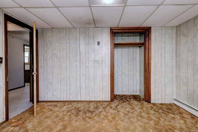 unfurnished bedroom with carpet floors, a baseboard radiator, a drop ceiling, and wood walls
