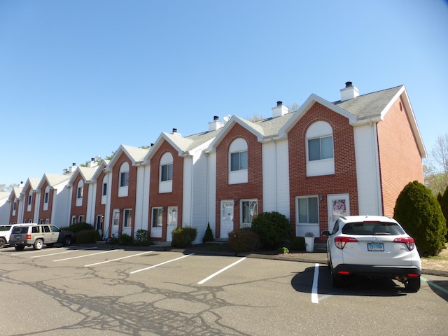 view of front of house with a chimney, uncovered parking, and brick siding