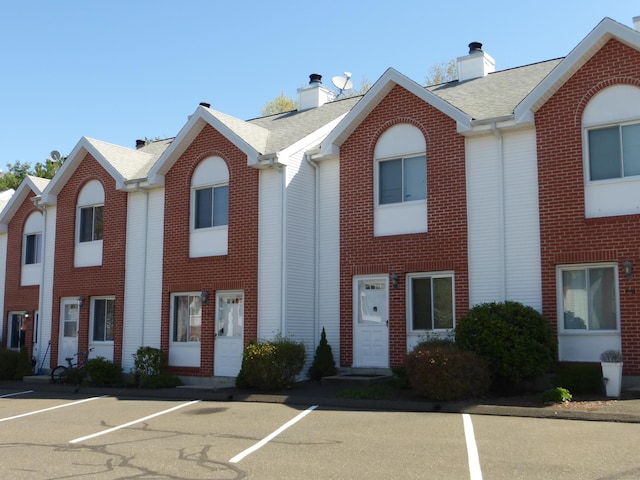 view of property featuring a chimney, brick siding, and uncovered parking