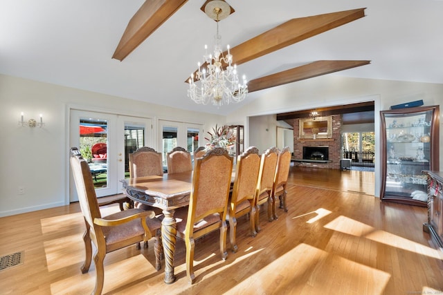 dining room featuring a brick fireplace, a chandelier, vaulted ceiling with beams, wood finished floors, and visible vents
