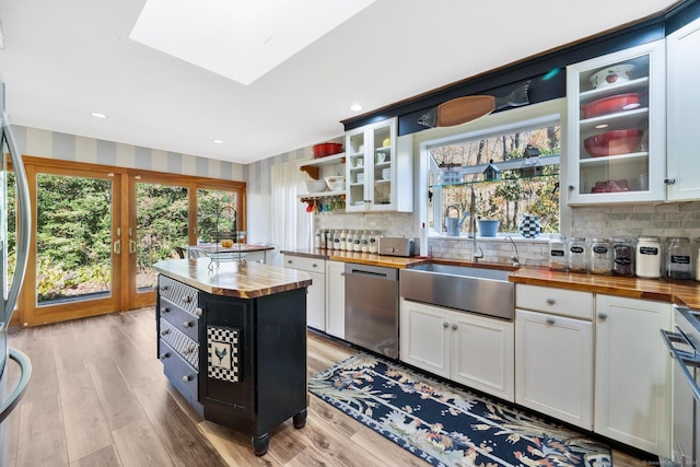 kitchen with open shelves, a sink, light wood finished floors, wood counters, and stainless steel dishwasher