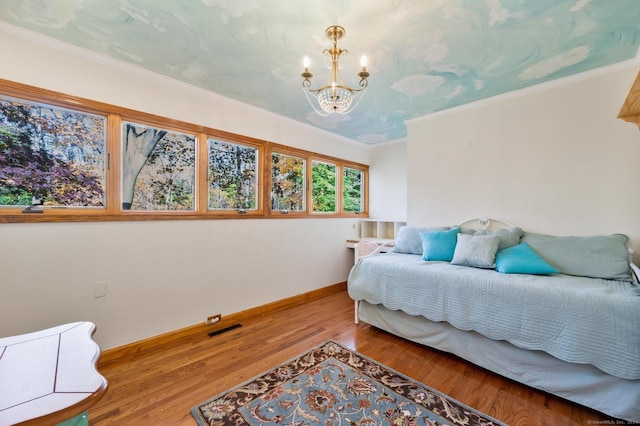 bedroom featuring visible vents, crown molding, wood finished floors, baseboards, and an inviting chandelier
