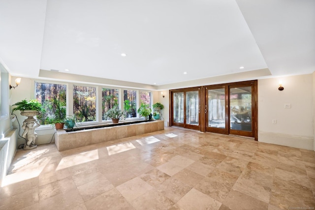 unfurnished living room featuring french doors, stone finish floor, a tray ceiling, and recessed lighting
