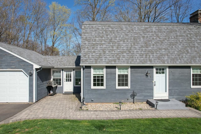 new england style home featuring an attached garage, a shingled roof, and a chimney