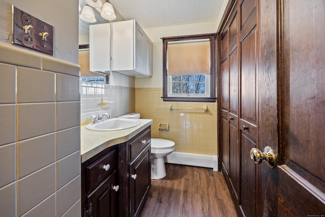bathroom with tile walls, baseboard heating, wood finished floors, vanity, and toilet