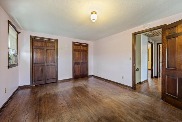 unfurnished bedroom with baseboards, cooling unit, two closets, and dark wood-type flooring