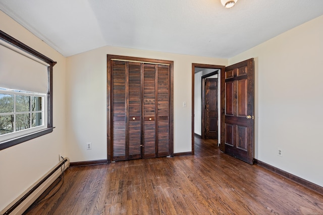unfurnished bedroom featuring wood finished floors, baseboards, a closet, a baseboard heating unit, and lofted ceiling