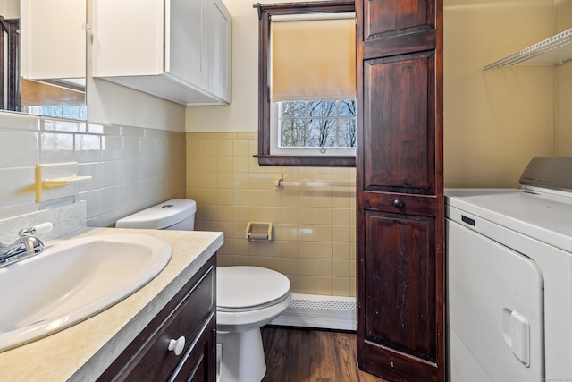 bathroom with toilet, washer / dryer, baseboard heating, and wood finished floors