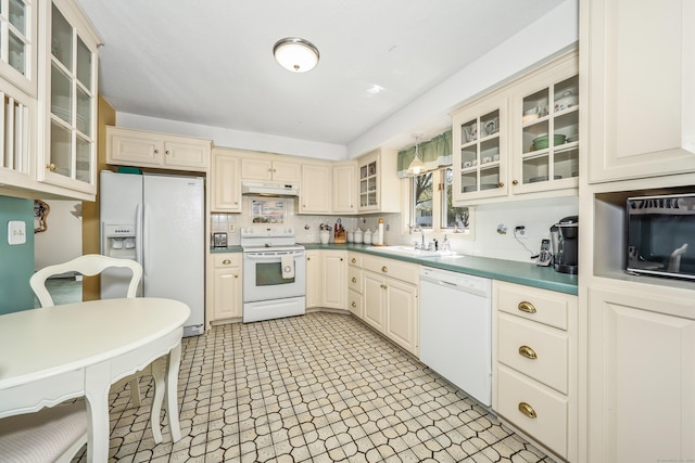 kitchen with white appliances, glass insert cabinets, under cabinet range hood, cream cabinets, and a sink
