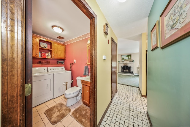 laundry room featuring visible vents, washing machine and dryer, a brick fireplace, cabinet space, and light tile patterned floors