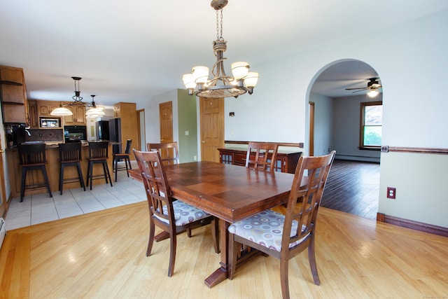 dining area with arched walkways, ceiling fan with notable chandelier, light wood-style floors, and a baseboard heating unit