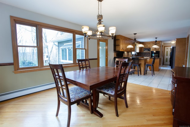 dining space with a baseboard radiator, light wood-style floors, and a notable chandelier
