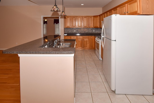 kitchen featuring light tile patterned flooring, dark countertops, a sink, white appliances, and backsplash