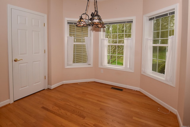 unfurnished dining area featuring visible vents, baseboards, a notable chandelier, and light wood-type flooring