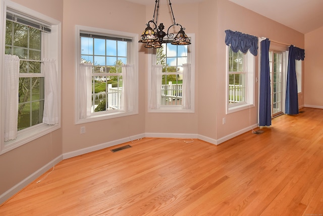 unfurnished dining area with baseboards, visible vents, wood finished floors, and a chandelier