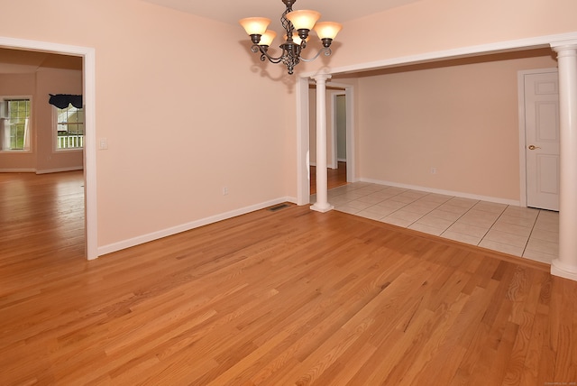 unfurnished room featuring decorative columns, an inviting chandelier, visible vents, and light wood-style floors