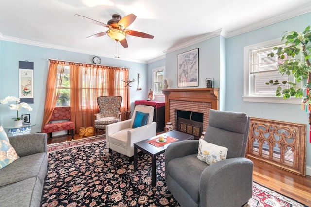 living room with a brick fireplace, a ceiling fan, ornamental molding, and wood finished floors