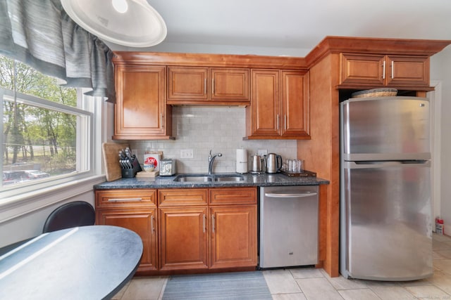 kitchen featuring brown cabinetry, light tile patterned flooring, tasteful backsplash, a sink, and stainless steel appliances