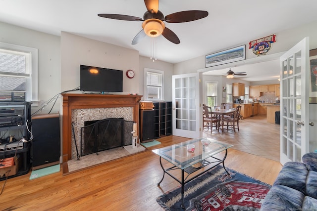 living area with french doors, a ceiling fan, light wood-style flooring, and a tiled fireplace