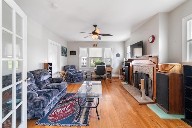 living room with a ceiling fan, light wood finished floors, and a fireplace