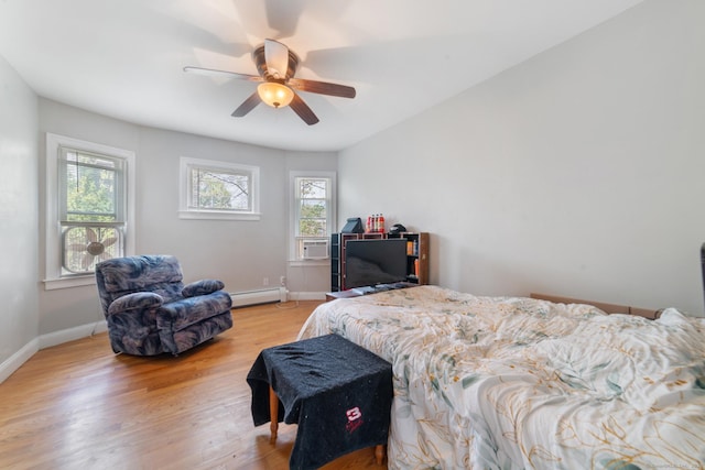bedroom with light wood-style floors, a ceiling fan, baseboards, and a baseboard heating unit