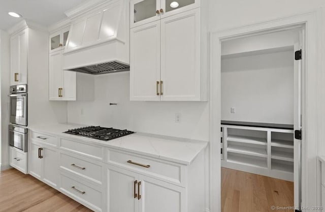 kitchen featuring light stone countertops, white cabinetry, gas stovetop, custom range hood, and light wood-type flooring