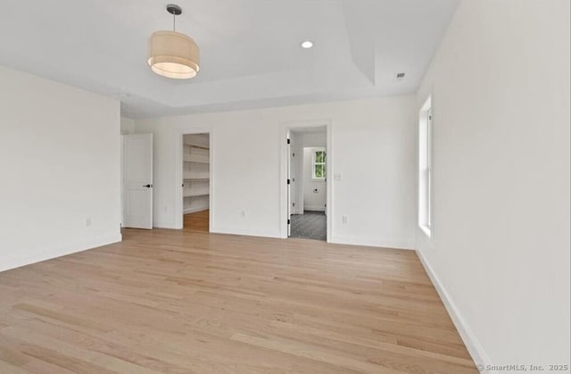 unfurnished room featuring light wood-style floors, a raised ceiling, and baseboards