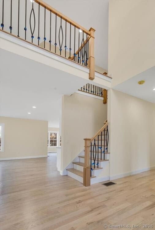stairs with wood finished floors, a towering ceiling, and recessed lighting