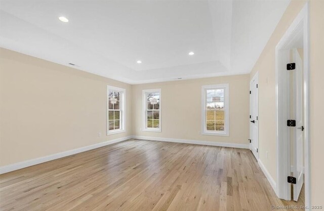 unfurnished room with light wood-type flooring, a raised ceiling, and recessed lighting