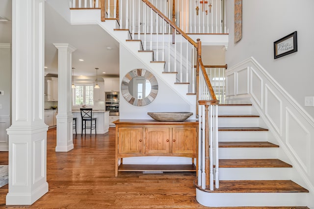 stairs featuring a high ceiling, decorative columns, and wood finished floors