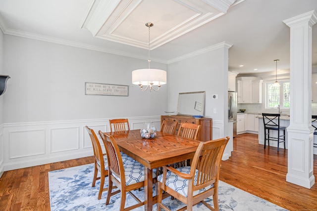 dining space with ornate columns, wainscoting, ornamental molding, and light wood-type flooring
