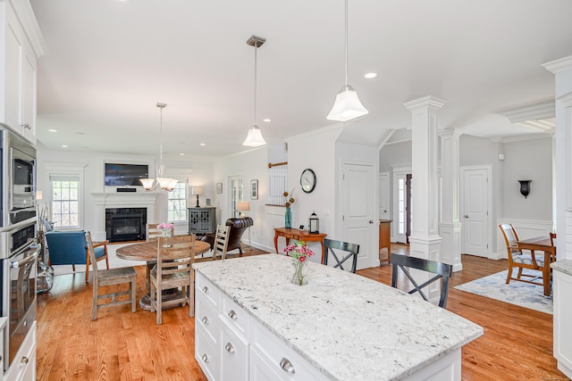 kitchen with appliances with stainless steel finishes, a glass covered fireplace, white cabinetry, open floor plan, and ornate columns