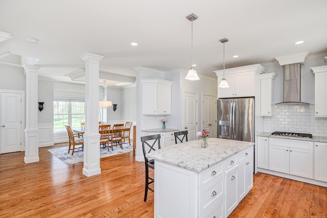 kitchen with wall chimney range hood, ornate columns, a center island, white cabinetry, and stainless steel appliances