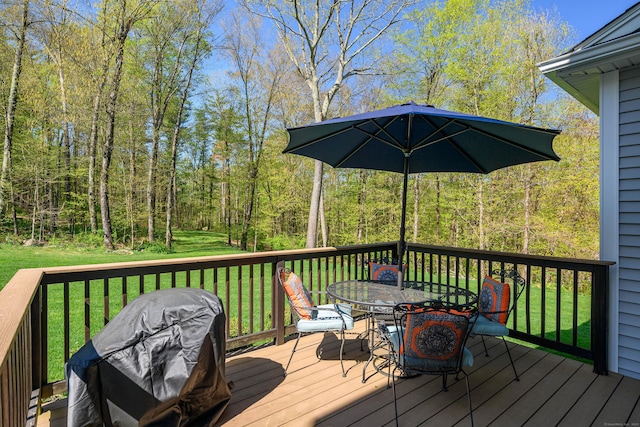 deck with a lawn, a wooded view, and outdoor dining space