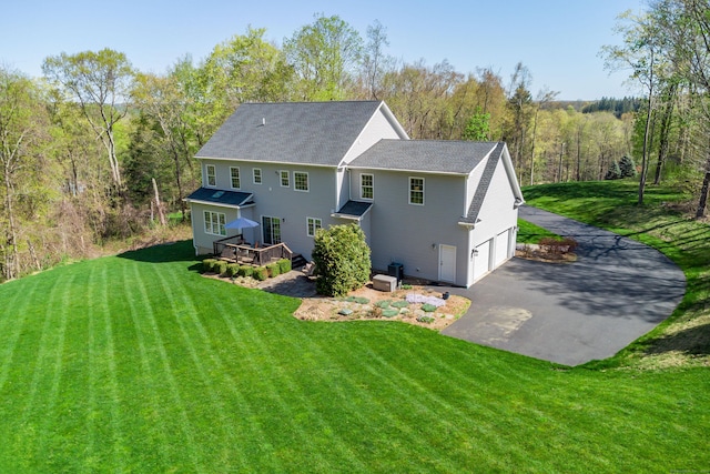 rear view of property with driveway, a wooden deck, a garage, a yard, and a shingled roof
